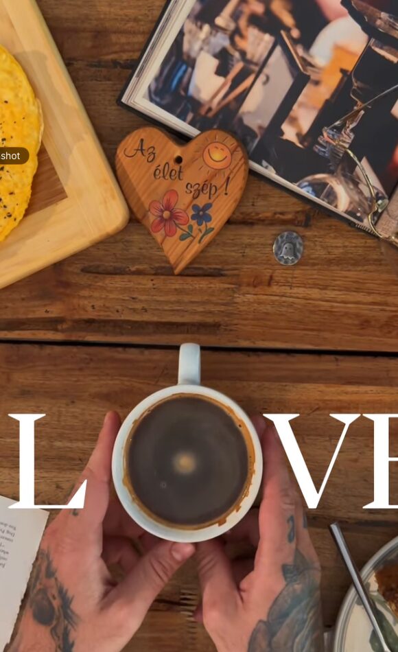 Taza de café Rev sobre mesa de madera · manos tatuadas sosteniéndola